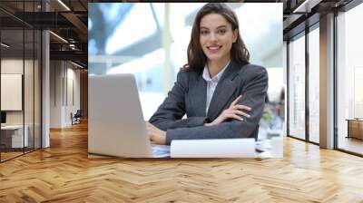 Portrait of a cheerful young businesswoman sitting at the table in office and looking at camera. Wall mural