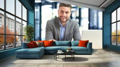 Portrait of happy businessman sitting at office desk, looking at camera, smiling. Wall mural