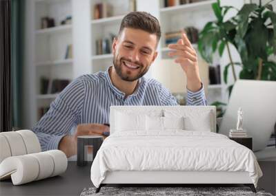 Smiling man sitting in office and pays by credit card with his laptop. Wall mural