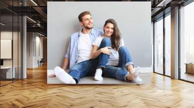 The happy couple sitting on the background of the gray wall. Wall mural