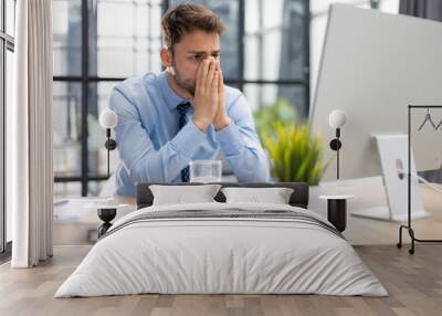 Unhappy frustrated young male holding head by hands sitting with computer behind desk at office. Wall mural