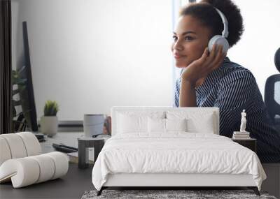 Young african american woman having a break and listening music in headphones sitting on working place. Wall mural