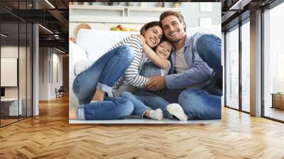 Young Caucasian family with small daughter pose relax on floor in living room, smiling little girl kid hug embrace parents, show love and gratitude, rest at home together. Wall mural