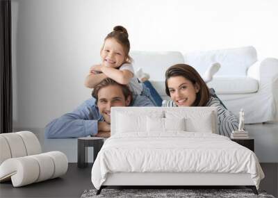 Young Caucasian family with small daughter pose relax on floor in living room, smiling little girl kid hug embrace parents, show love and gratitude on a transparent background Wall mural