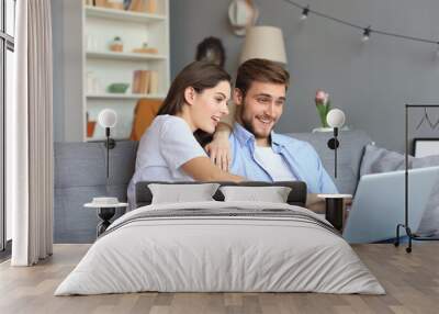 Young couple doing some online shopping at home, using a laptop on the sofa. Wall mural