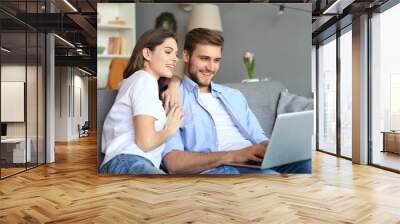 Young couple doing some online shopping at home, using a laptop on the sofa. Wall mural