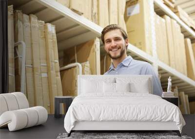 Young man shopping or working in a hardware warehouse standing checking supplies on his tablet. Wall mural