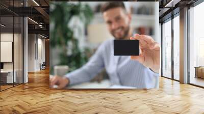 Young man sitting in office and pays by credit card with his tablet. Wall mural