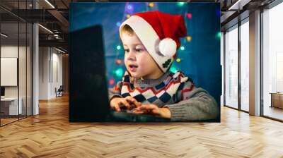 Little child writing letter to Santa Claus on laptop computer. Little boy with santa hat. Wall mural