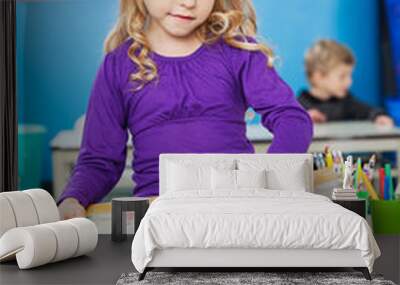 Girl Reading Book While Sitting On Desk At Kindergarten Wall mural