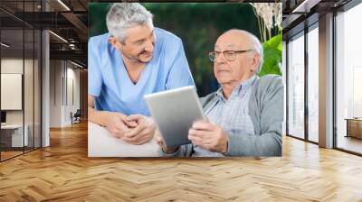 Male Caretaker Looking At Senior Man Using Tablet Computer Wall mural