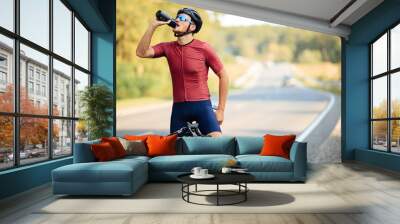 Muscular cyclist relaxing on bike and drinking water Wall mural