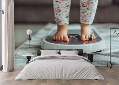 Close-up of a child's bare feet standing on a digital scale, showcasing their tiny toes and a focused expression on their face. Wall mural