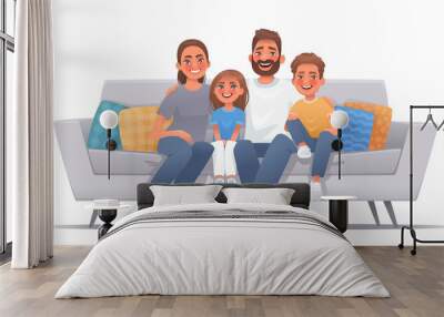 Happy family sitting on sofa over isolated background. Mom, dad, son and daughter are smiling while sitting on the couch. Concept of happiness and love, home comfort Wall mural