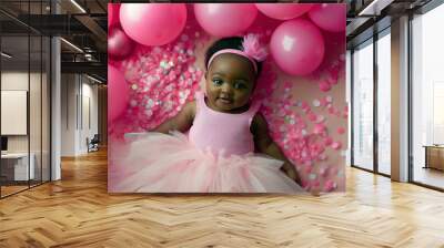 African-American baby girl wearing a tutu skirt and pink top, lying on her back surrounded by pink balloons and confetti. Wall mural