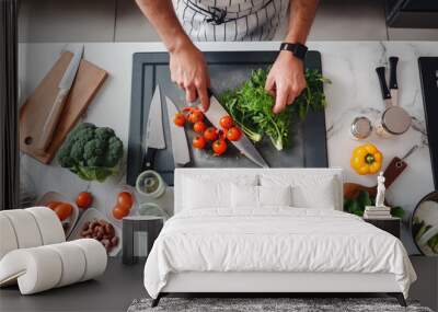 Point-of-view of a person chopping vegetables on a cutting board, with various fresh ingredients and cooking utensils on a kitchen countertop. Wall mural