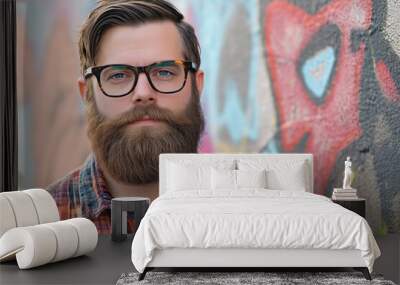 Portrait of a hipster with a beard and trendy glasses in front of a graffiti-covered wall. Wall mural