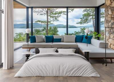 A modern outdoor lounge featuring light grey and white wood walls, blue accent pillows on the sofa, a large window overlooking the ocean, stone wall accents, and white concrete flooring is created. Wall mural