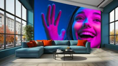 This is a portrait of a smiling young woman expressing happiness and excitement against a gradient blue studio background in neon light. Banner. Ad, text space available. Wall mural