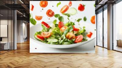 Salad with fresh vegetables and avocado falling into a plate on white background Wall mural