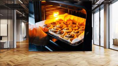 Baker wearing protective glove and checking her cinnamon rolls in the oven Wall mural