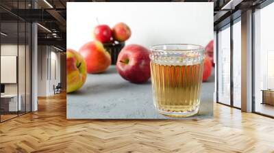 Lot of ripe tasty apples adn glass of apple juice on the grey surface against white wall Wall mural