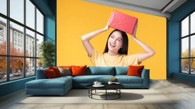 Portrait of happy smiling girl in casual holding gift box and expression face isolated over yellow background Wall mural