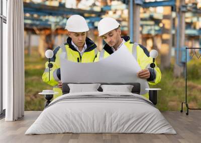 Engineers with a construction plan working near high-voltage powerline. Two engineers in special clothing discuss a drawing on paper against the background of a high-voltage power line Wall mural