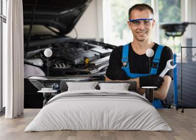 Portrait of european caucasian car mechanic in uniform with tools in his hands looks at the camera and laughs happily. Car service concept Wall mural