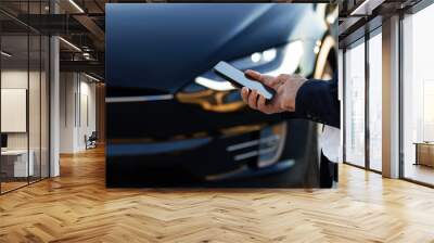 Unrecognizable elegant man using smartphone app for remote controlling of premium class Tesla Plaid car, driver distantly approaching car and opening door, smart car Wall mural