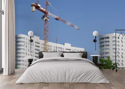 Red construction crane on a background of white buildings and blue sky. Wall mural