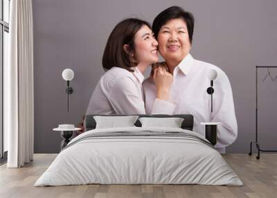 Beautiful senior mom and her adult daughter are hugging, looking at camera and smiling Wall mural