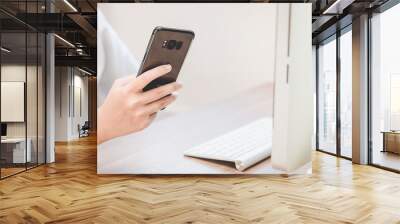 Hand holding black smart phone on back view in workspace Wall mural