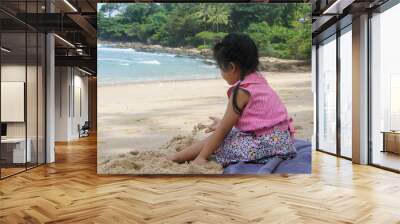 side view of a little cute girl dress casually sitting on the beach playing sand. Holiday, family, healthy child concept Wall mural