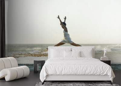 A beautiful young black woman leaps through the air as waves crash around her Wall mural