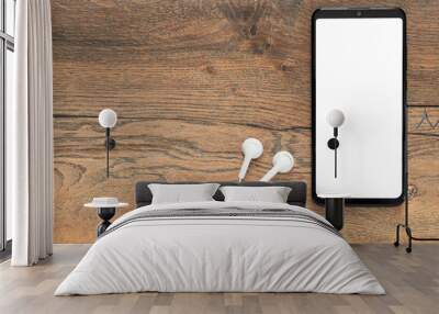 Smartphone with isolated white screen with connected earphones on the background of a wooden desk Wall mural