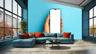 Empty smartphone in hand on colored blue banner background. Mockup phone with blank screen on minimal background Wall mural