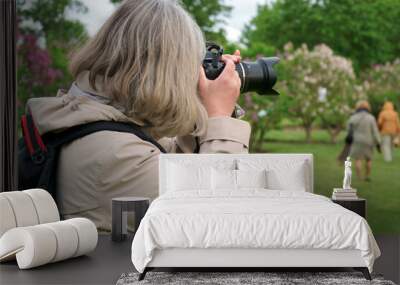 Events reportage photographer in action. A photojournalist with a camera takes travel tour photos in nature. The wonderful moments when the lilac trees are blooming in Latvia. Wall mural