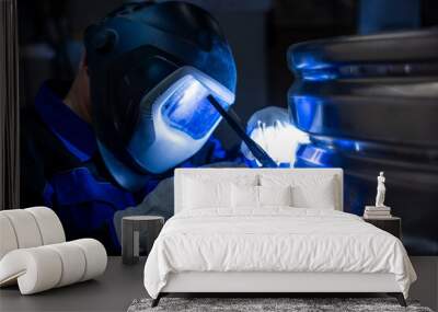 Welder in protective gear focused on welding a metal structure in a dimly lit workshop, highlighting the welding process. Wall mural