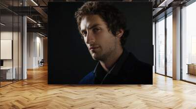 Handsome young brunette man with light eyes in dark clothes looks into the distance. Wall mural