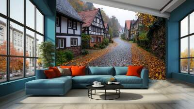 Quiet countryside village with timber-framed houses, a cobblestone street winding through, autumn leaves on the ground, soft morning light, traditional German architecture. Wall mural