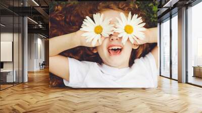 Child with daisy eyes, on green grass in a summer park. Wall mural