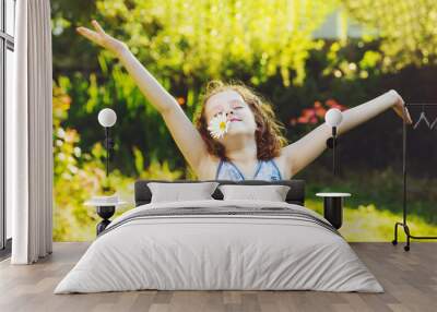 Little curly girl with daisy in her teeth resting in spring park. Wall mural