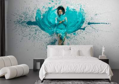 expressive sexy woman lies naked elegant on the floor in turquoise blue color abstract painted bodypainting woman on the splashed ground, spreads the paint in form of angel wings Wall mural