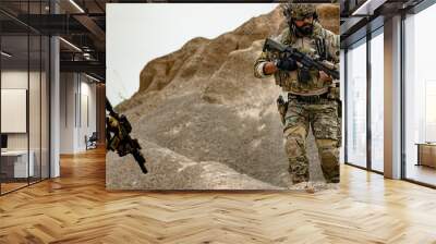 A group of military men in combat gear patrol in the middle of a desert and tropical jungle. Soldiers in full combat gear in dry weather conditions assemble and march on a mission. Wall mural