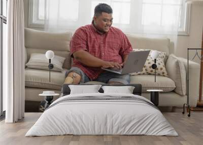 Asia man working with tablet in a sofa in the living room. male with mechanic steel leg sitting and writing on a digital tablet device. Wall mural