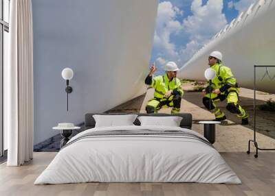 engineers in high visibility safety gear conduct a detailed inspection of a wind turbine blade at a construction site. The massive blade lays on the ground, highlighting renewable energy technology. Wall mural