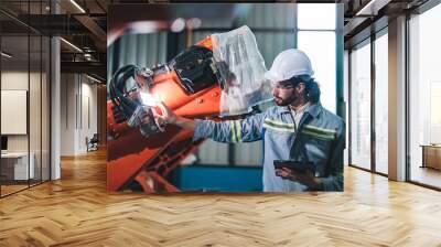 Factory engineer inspecting on machine with smart tablet. Worker works at heavy machine robot arm. The welding machine with a remote system in an industrial factory. Artificial intelligence concept. Wall mural