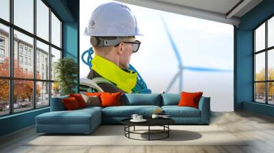 Two engineers in high visibility gear and hard hats observe a wind turbine and communicate via radio at a wind energy site. The image highlights teamwork, safety, and renewable energy production. Wall mural