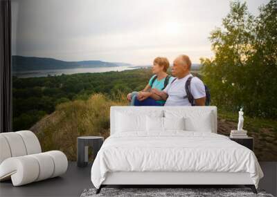 elderly couple with backpacks sits on the mountain. Senior couple walking in nature. travel tourism concept Wall mural